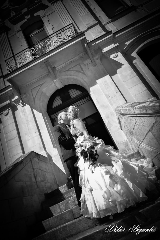@photographe.mariage.portraits.aveyron photo en noir et blanc d'un couple de jeune marié qui s'embrasse sur l'escalier de la mairie du village d' Aubin proche de Decazeville en Aveyron ils viennnent de sortir de la marie