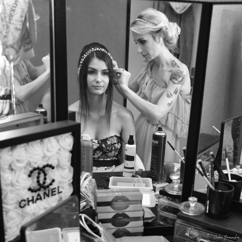photo en noir et blanc d"une future mariée lors des préparatifs en train de ce faire coiffée par la coiffeuse qui lui pose un diademe 