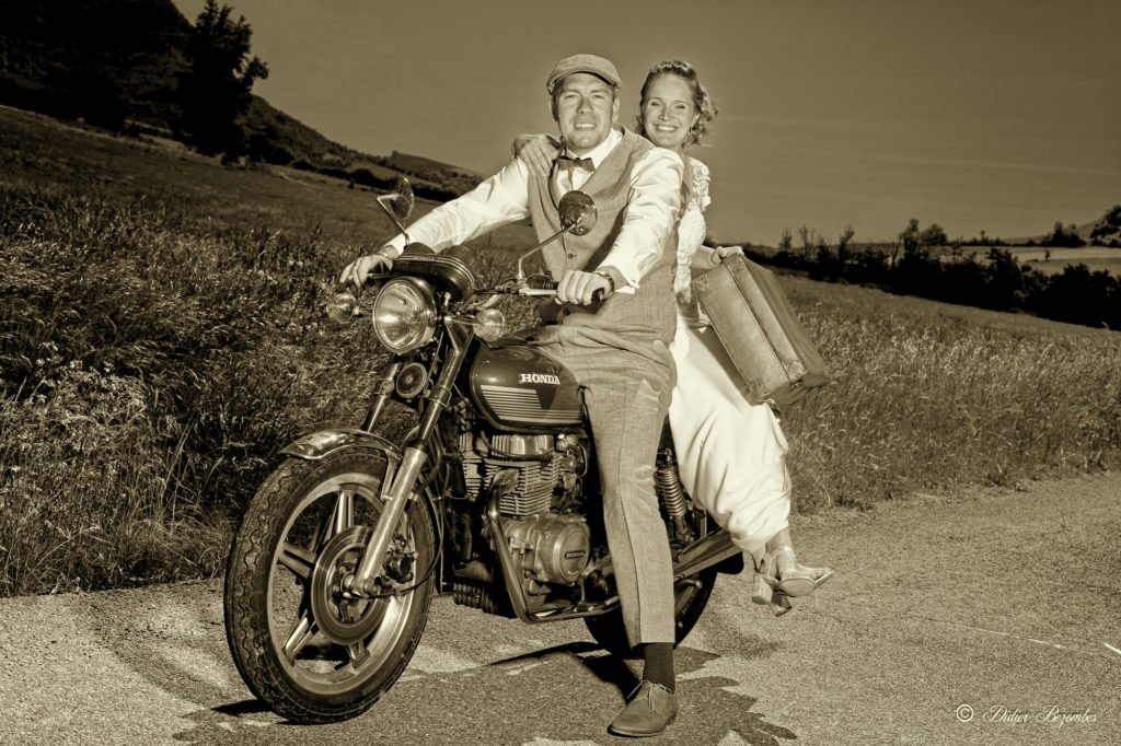 photos de mariage retro en aveyron sur le theme annees 1970 .la photo est en ton sépia les mariées sont assis sur moto de marque Honda