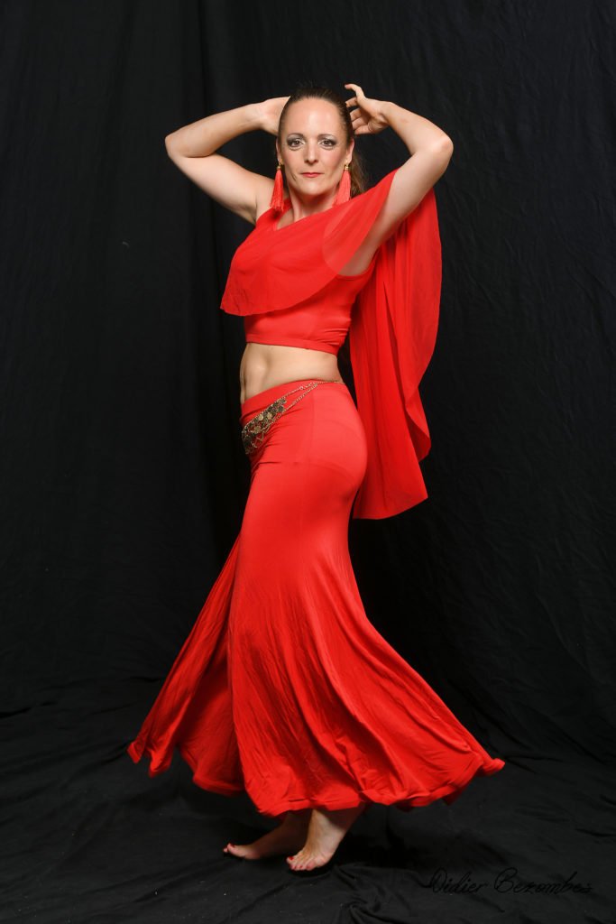 photo en studio de 1 danseuse orientale le fond est noir elle une robe rouge la danseuse est très souriante elle a été photographier par Didier Bezombes photographe à Rodez en Aveyron