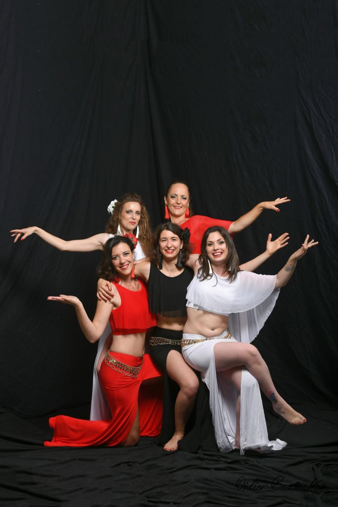 photo en studio de 5 danseuses orientale le fond est noir il y en n'à 2 avec une robe rouge et 2 robes blanche et une en robe noir les danseuses sont souriantes elles on été photographier par Didier Bezombes photographe à Rodez en Aveyron